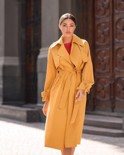 Woman wearing a yellow trench coat standing in front of an ornate door.