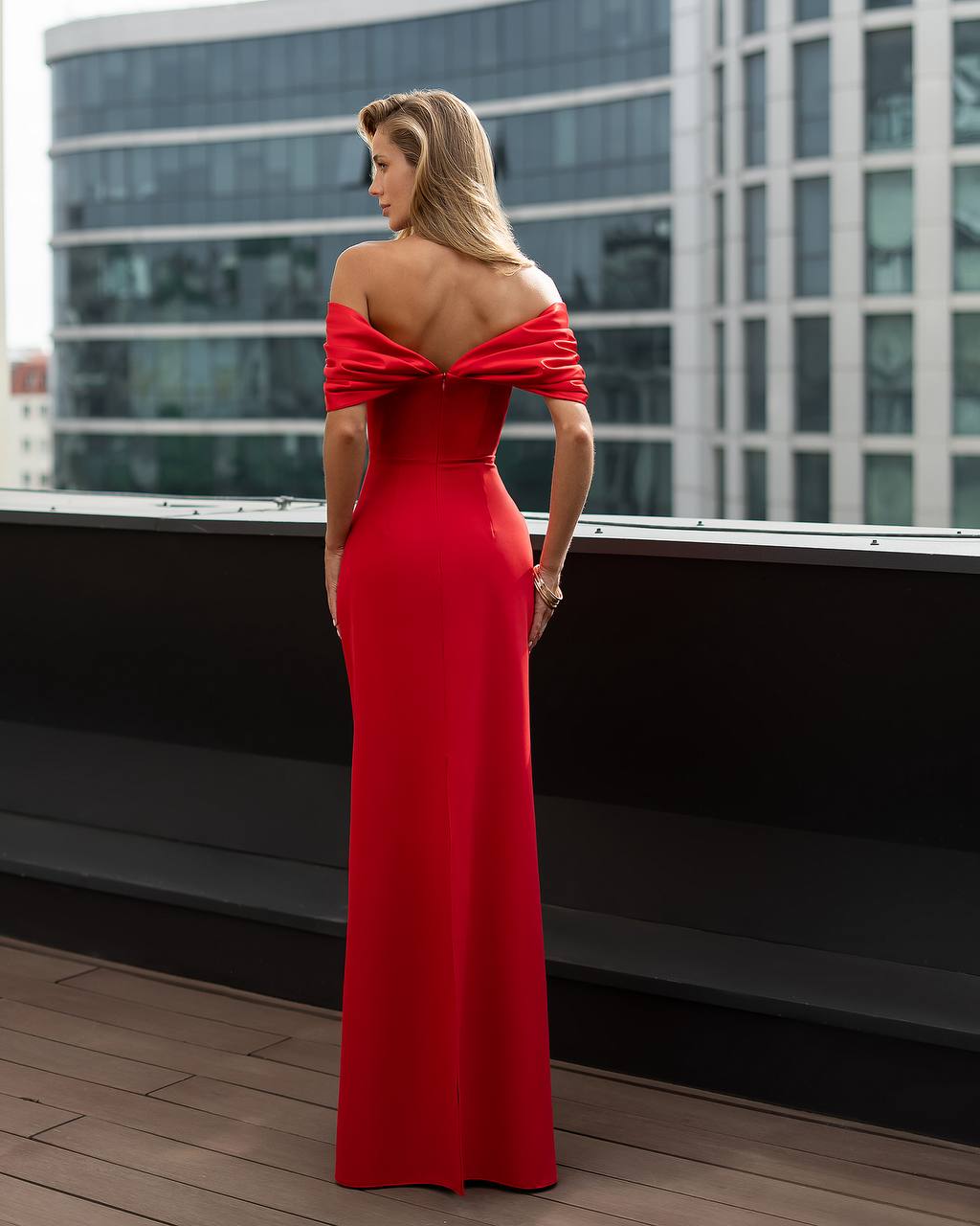 Woman in a red off-shoulder gown standing on a rooftop with cityscape background