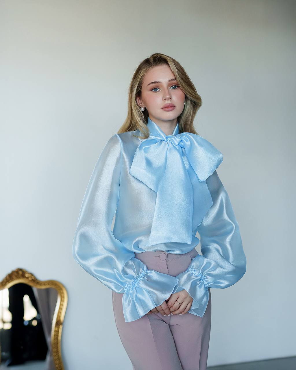 Woman wearing a light blue blouse with a large bow tie against a plain background
