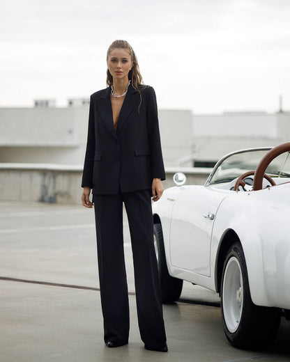 Woman in a black suit standing next to a white vintage car on a rooftop.