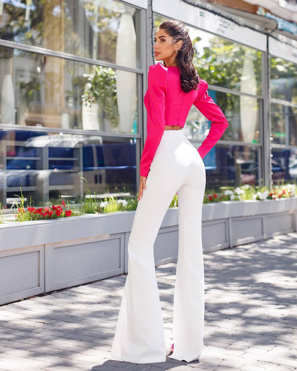 Woman wearing a bright pink top and white pants standing outdoors.