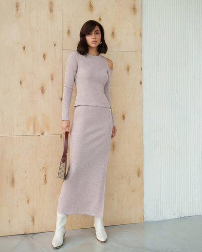 Woman wearing a light gray outfit standing against a wooden wall.
