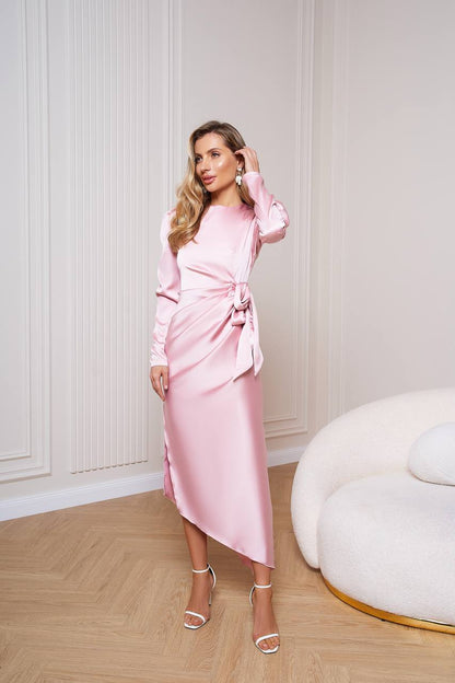 Woman in a pink dress standing in a stylish room with a white wall and modern furniture.