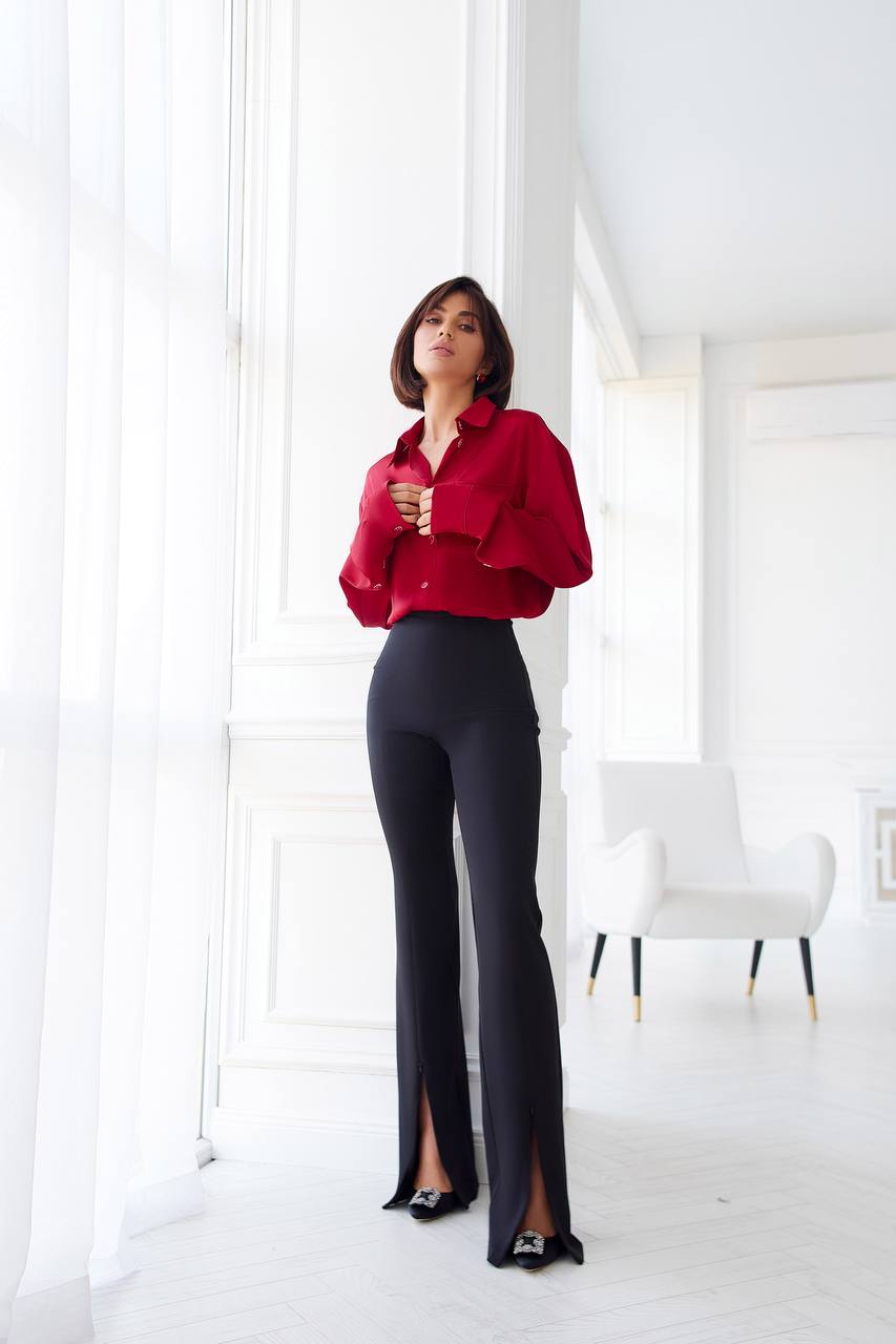 Woman wearing a red blouse and black pants in a bright room.