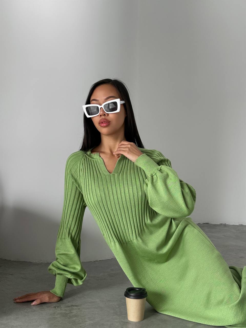 Woman in a green dress sitting on the floor with a coffee cup next to her.