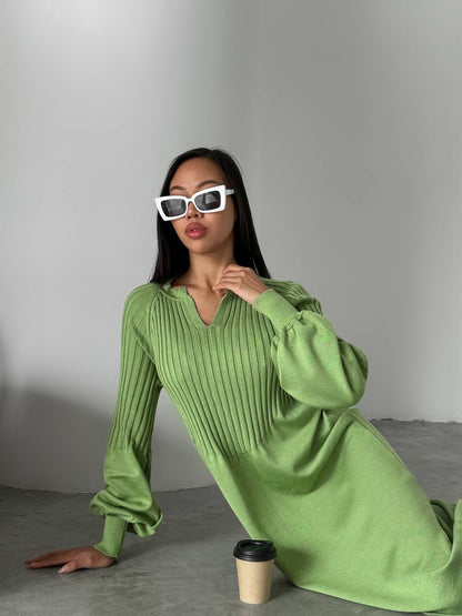 Woman in a green dress sitting on the floor with a coffee cup next to her.
