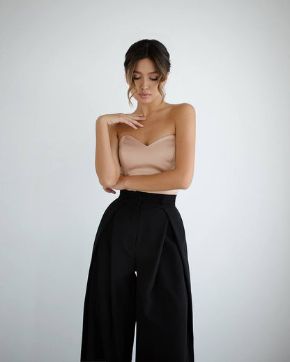 Woman wearing a strapless beige top and black high-waisted pants on a light gray background