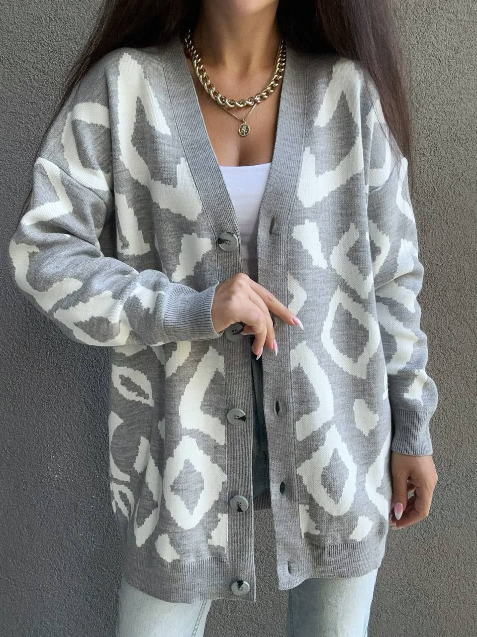 Person wearing a gray cardigan with a white geometric pattern against a plain background