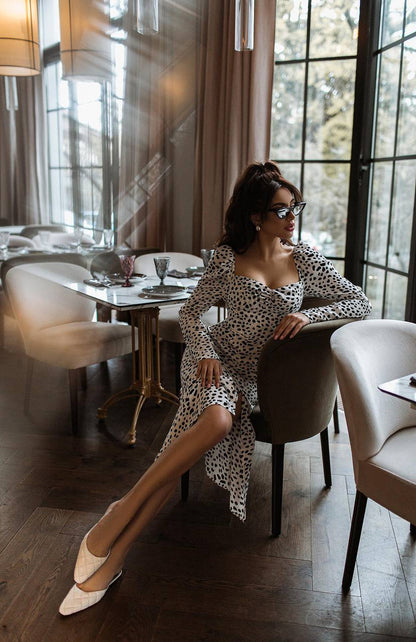Woman in a leopard print dress sitting in a stylish restaurant.