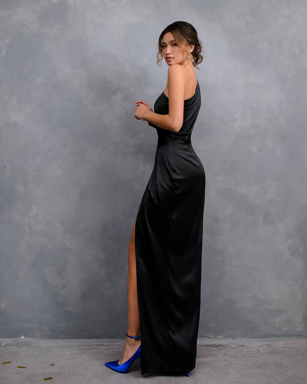 Woman wearing a black evening gown with a high slit against a gray background