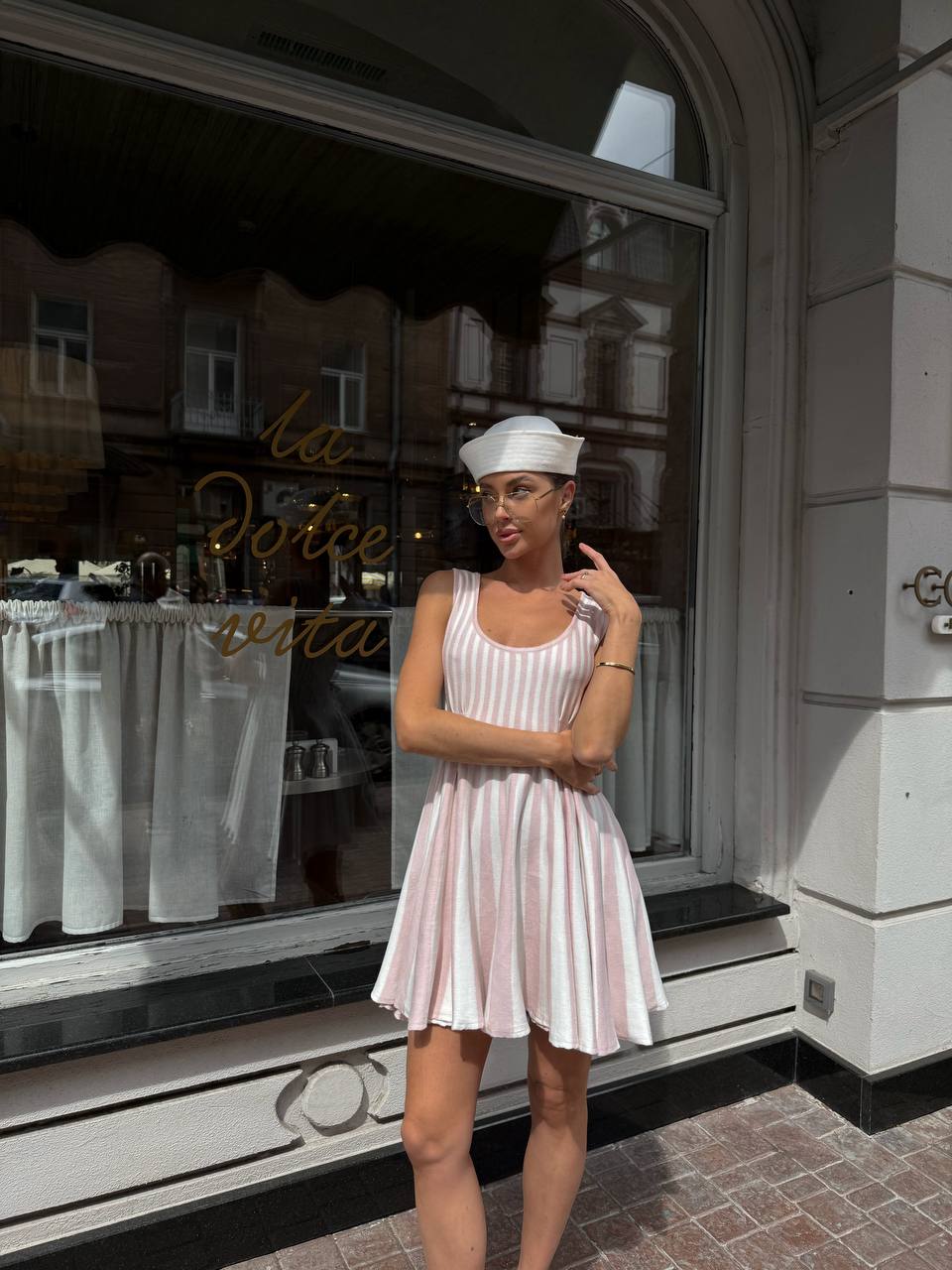 Woman in a white dress and cap standing in front of a store window.