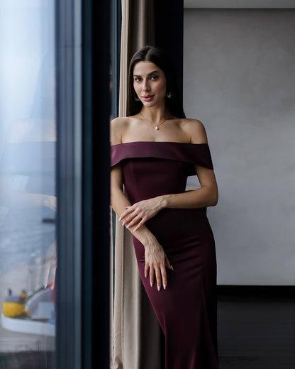 Woman in a burgundy off-shoulder dress standing indoors.