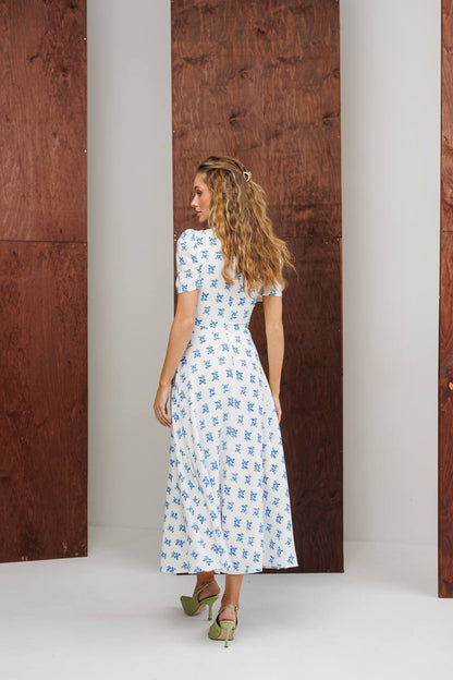 Woman in a floral dress standing in front of a wooden door.