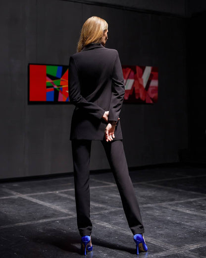 Woman in a black suit standing in front of abstract art in a dark room