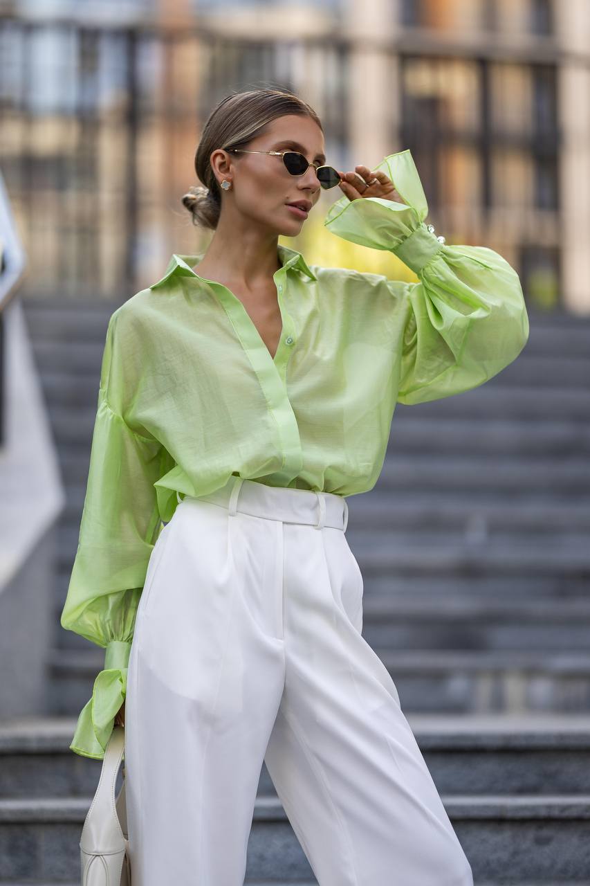 Person wearing a bright green shirt and white pants outdoors.