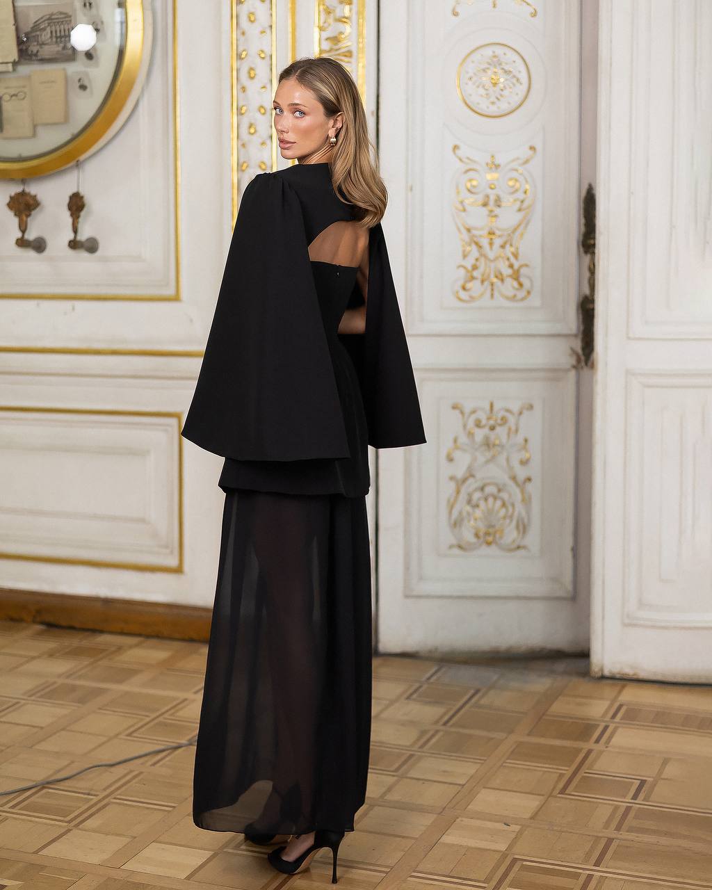 Woman in a black outfit standing in an ornate room with gold accents.