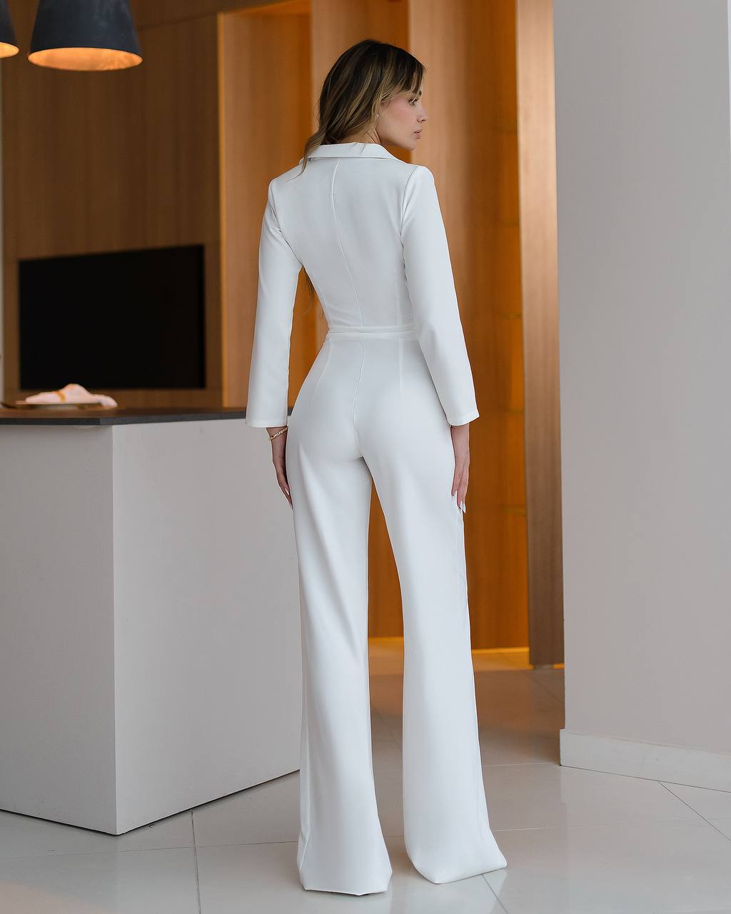 Woman wearing a white suit standing in a modern interior setting.