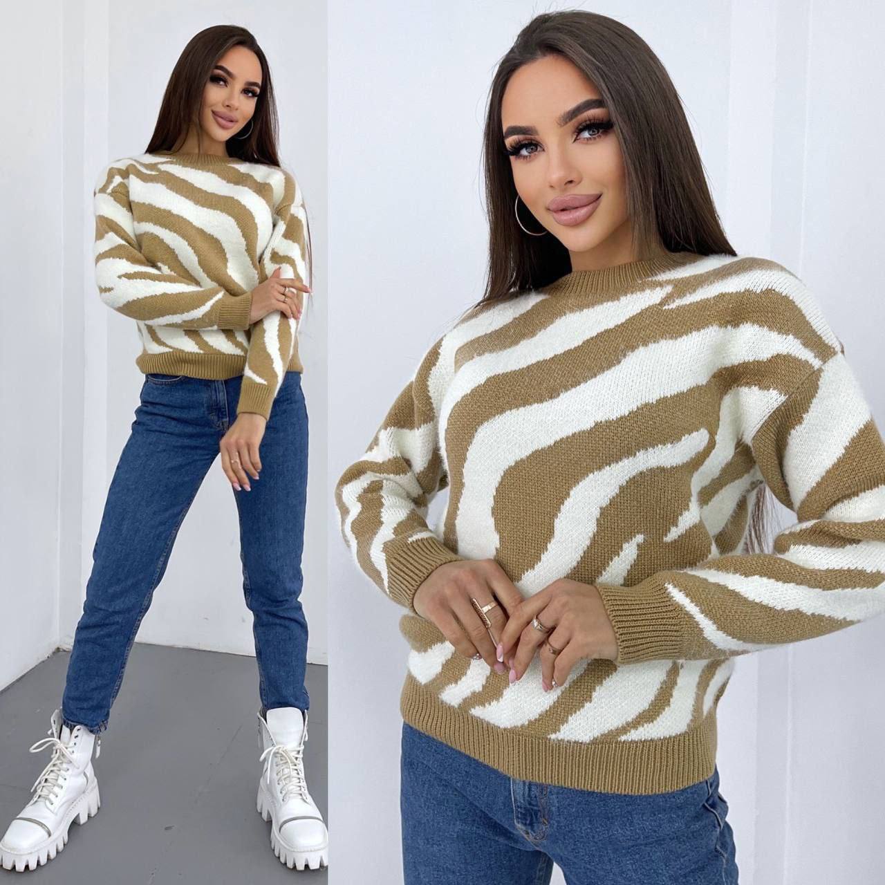 Woman wearing a brown and white patterned sweater with blue jeans against a white background