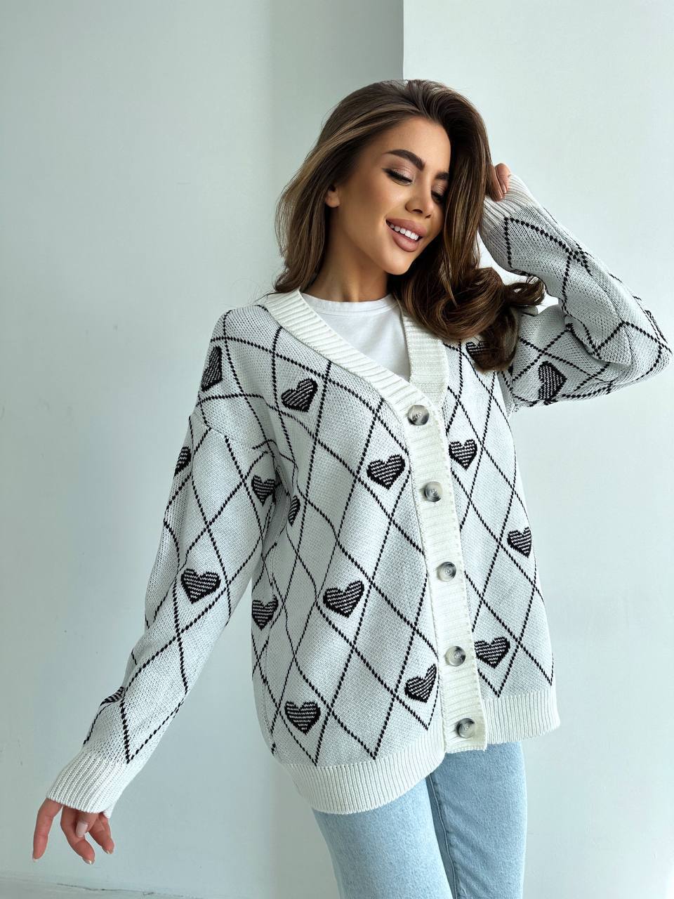 Woman wearing a white cardigan with black heart patterns against a light background