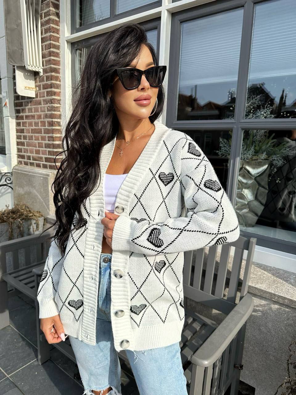 Woman wearing a white cardigan with black heart patterns outdoors.