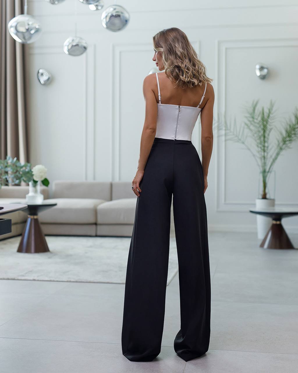 Woman wearing a white top and black pants in a modern living room.