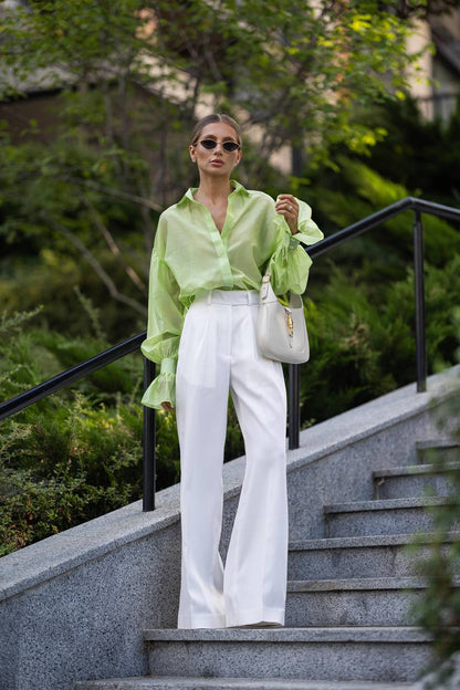 Woman in a light green shirt and white pants standing on steps outdoors.