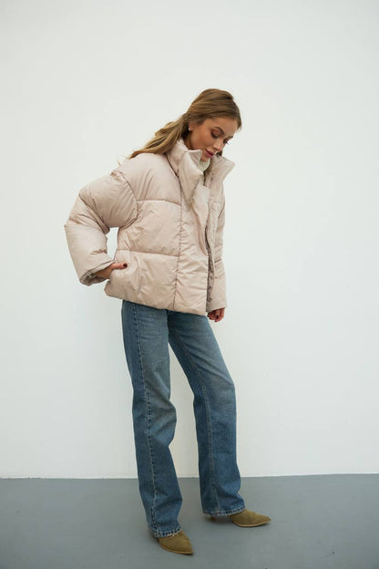Person wearing a beige puffer jacket and blue jeans against a white background