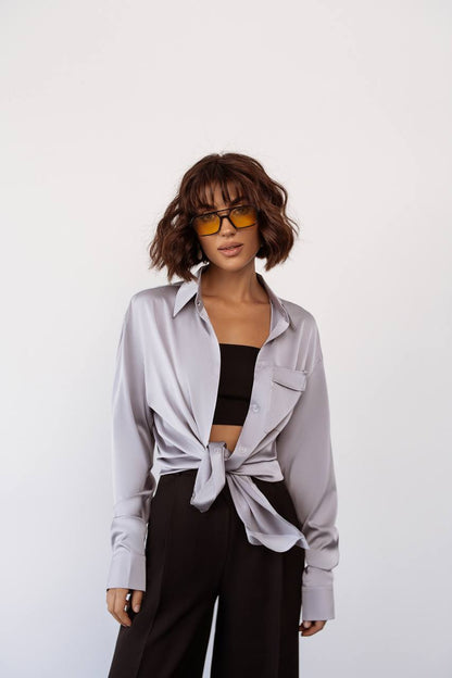 Woman wearing a light gray shirt tied at the waist with black pants on a white background