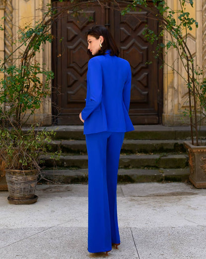 Woman in a blue suit standing in front of a decorative door with plants around.