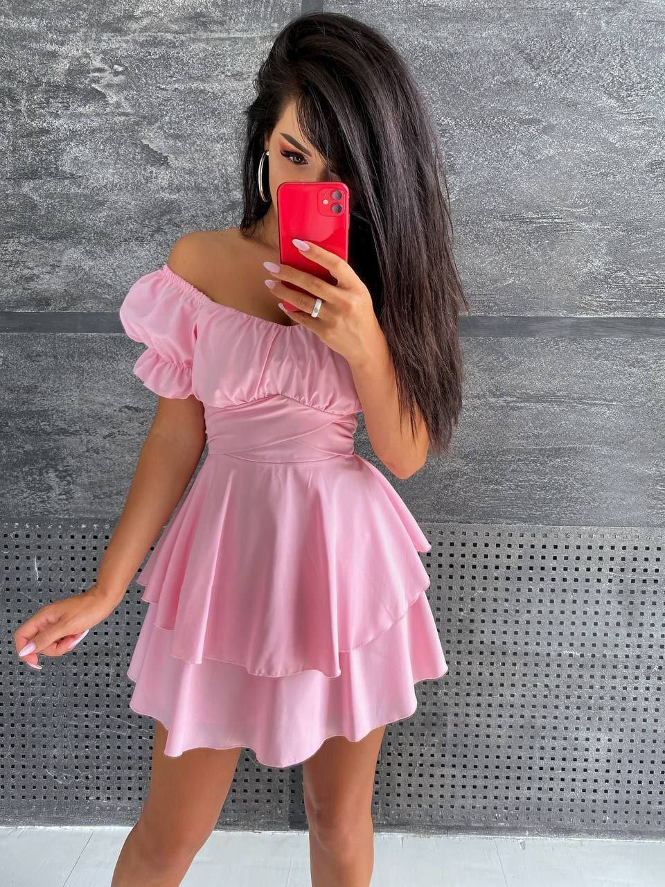 Woman wearing a pink off-shoulder dress against a gray textured wall.