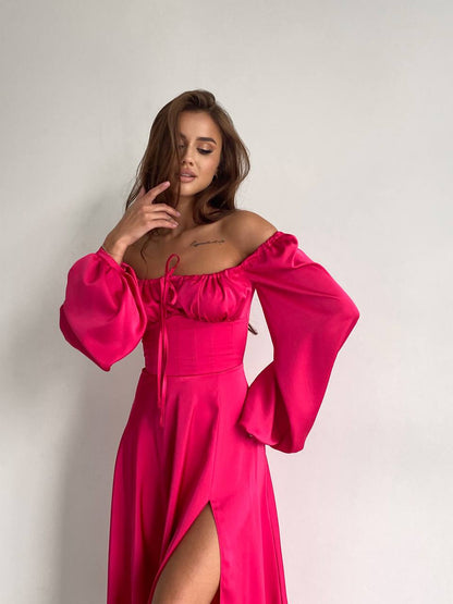 Woman wearing a bright pink off-shoulder dress with wide sleeves on a plain background