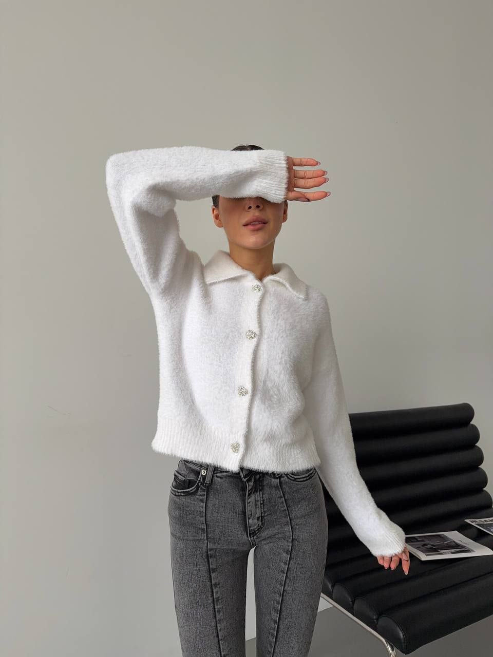 Person wearing a white sweater and gray jeans standing against a plain background