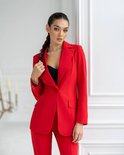 Woman wearing a red suit standing against a white wall.