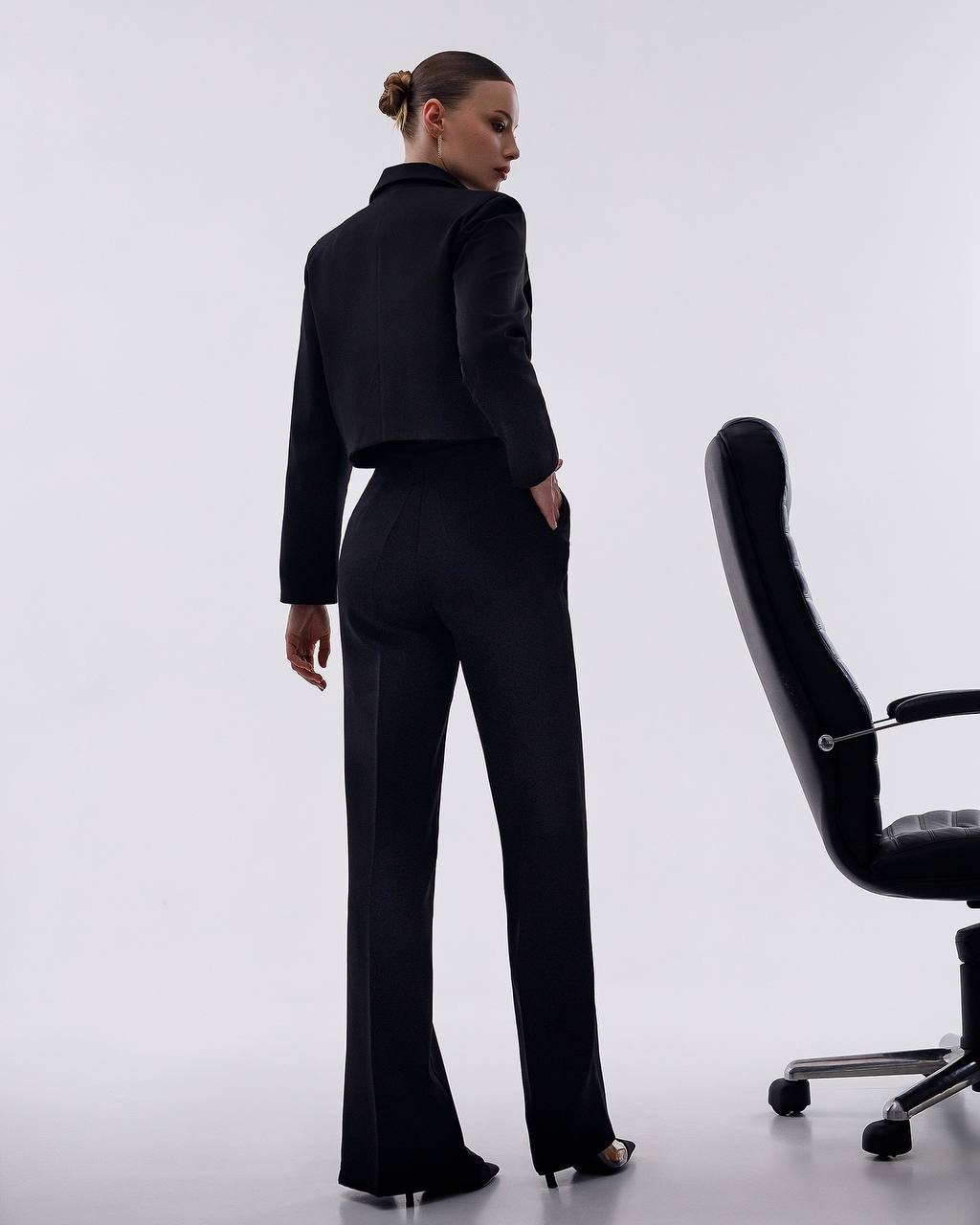 Person wearing a black outfit standing next to a black office chair on a white background