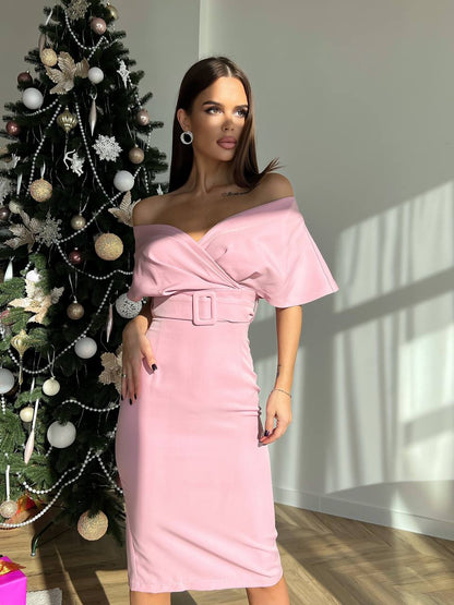 Woman in a pink off-shoulder dress standing next to a decorated Christmas tree.