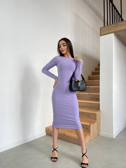 Woman in a purple dress standing in a room with wooden stairs.