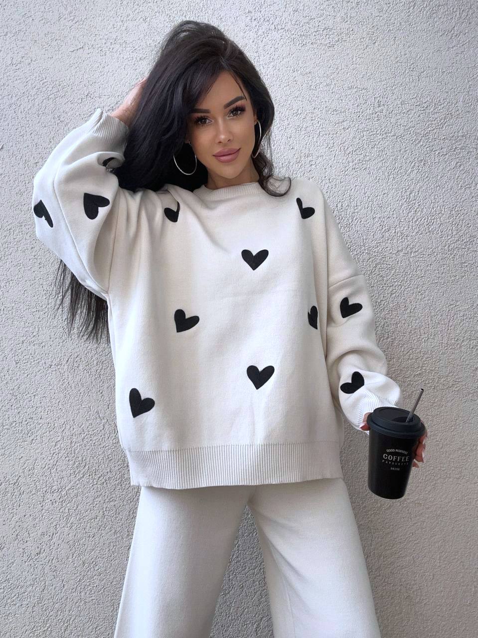 Woman wearing a white sweater with black heart patterns against a plain background