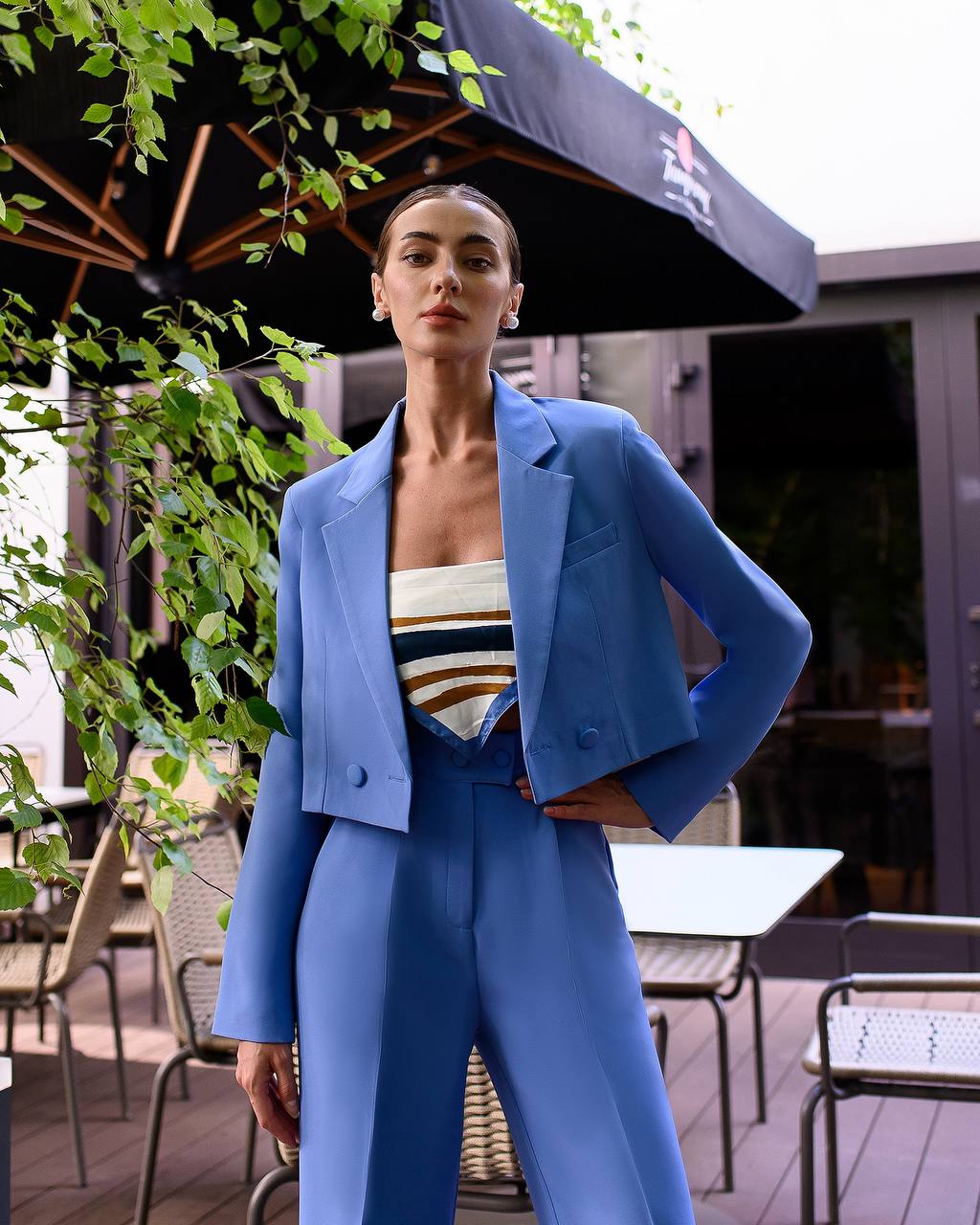 Woman in a blue suit standing outdoors with greenery and tables in the background
