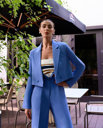 Woman in a blue suit standing outdoors with greenery and tables in the background