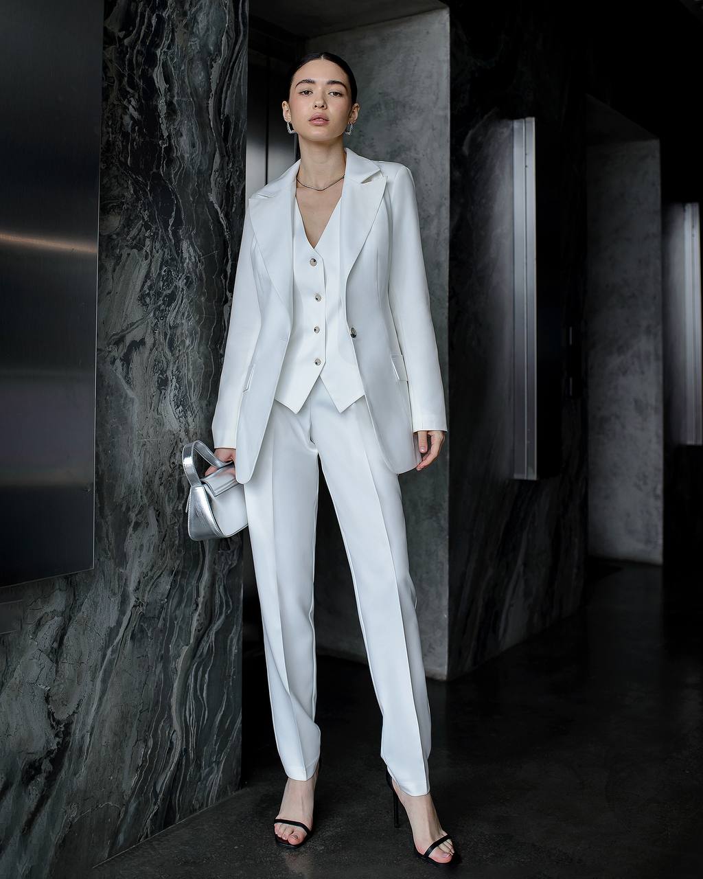 Woman in a light gray suit standing in a dark room with marble walls.