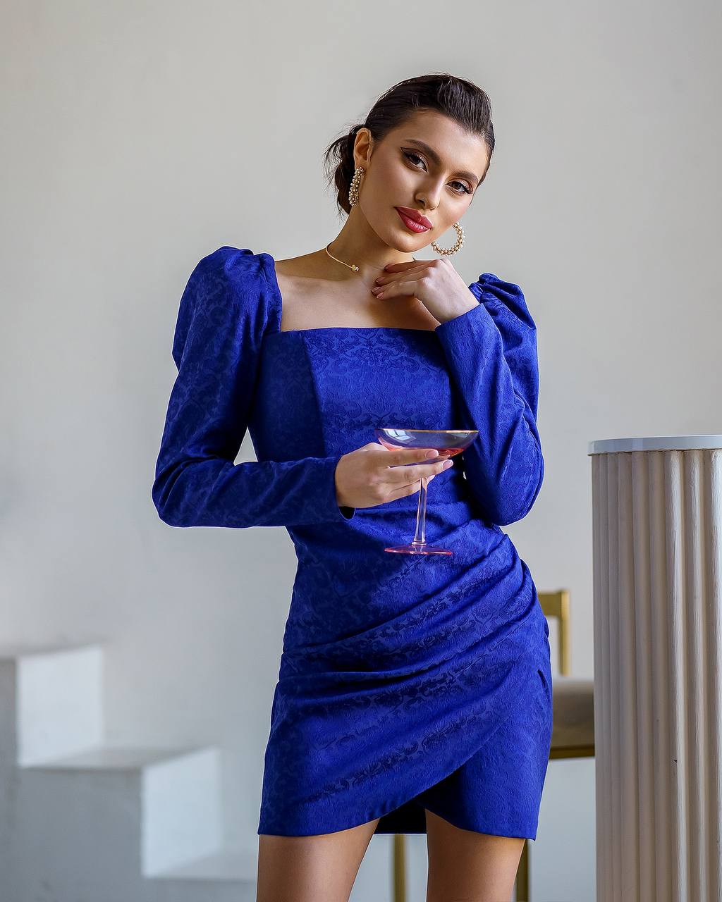 Woman in a blue dress holding a glass in an indoor setting