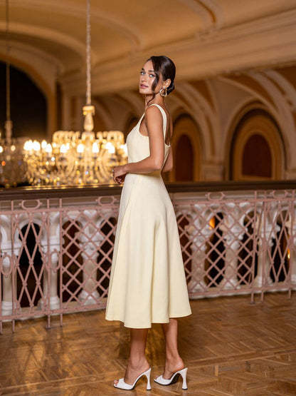 Woman in a light yellow dress standing in an elegant indoor setting with chandeliers.