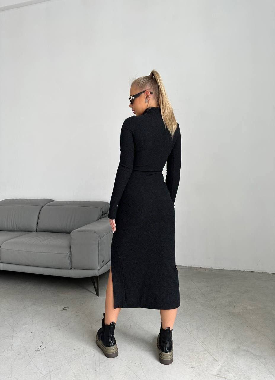 Woman wearing a black dress standing in a minimalistic room with a gray sofa.
