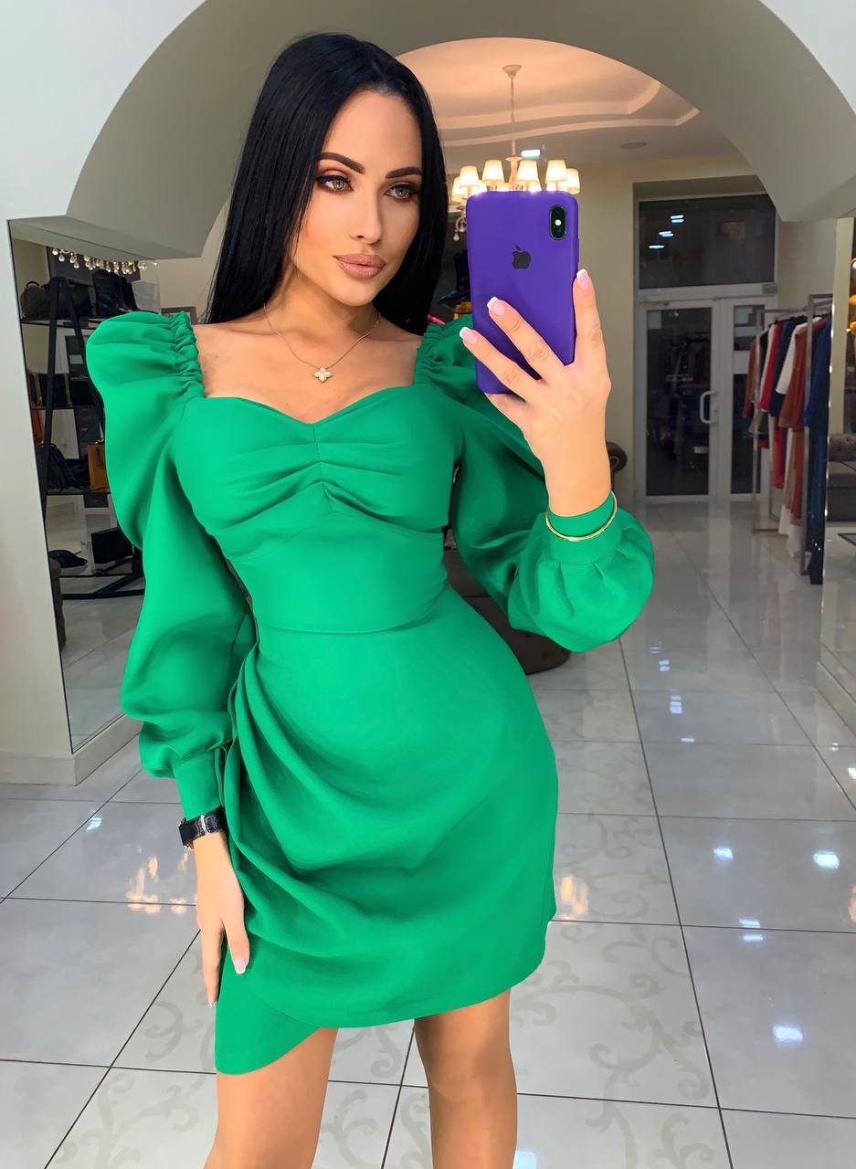 Woman taking a mirror selfie wearing a green dress in a mall setting.