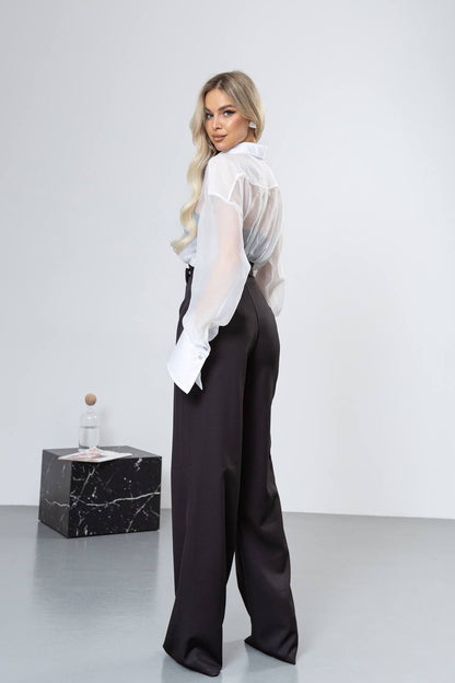 Woman wearing a white blouse and black pants against a plain background