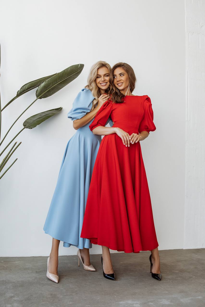Two women in blue and red dresses standing next to each other against a white wall.