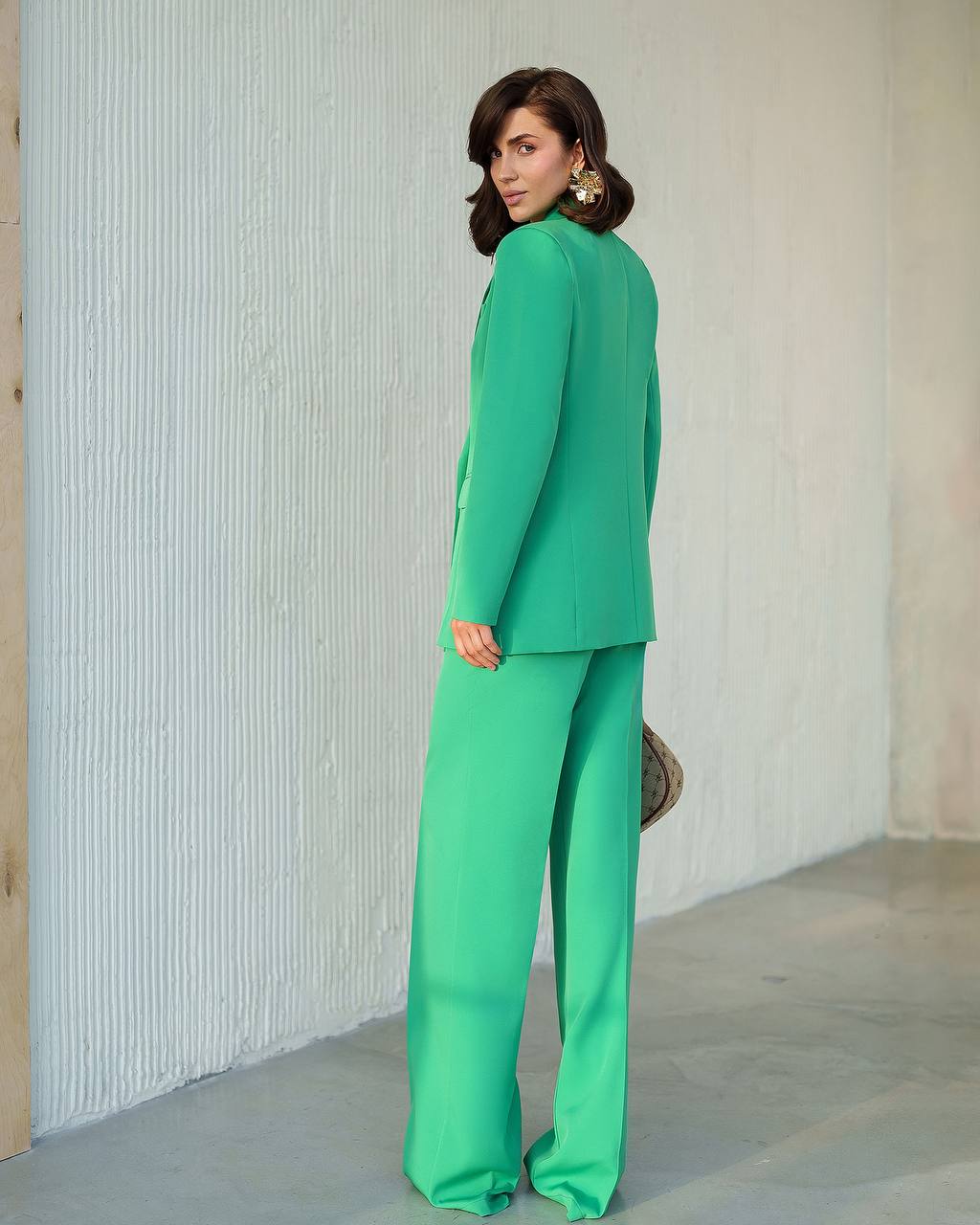 Woman wearing a green suit standing against a light-colored wall.