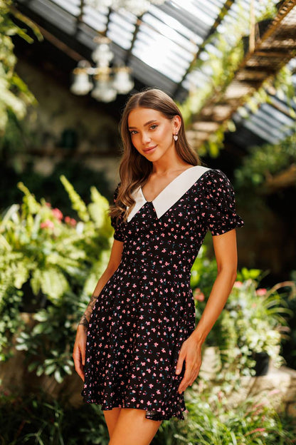 Woman in a black floral dress standing in a garden setting
