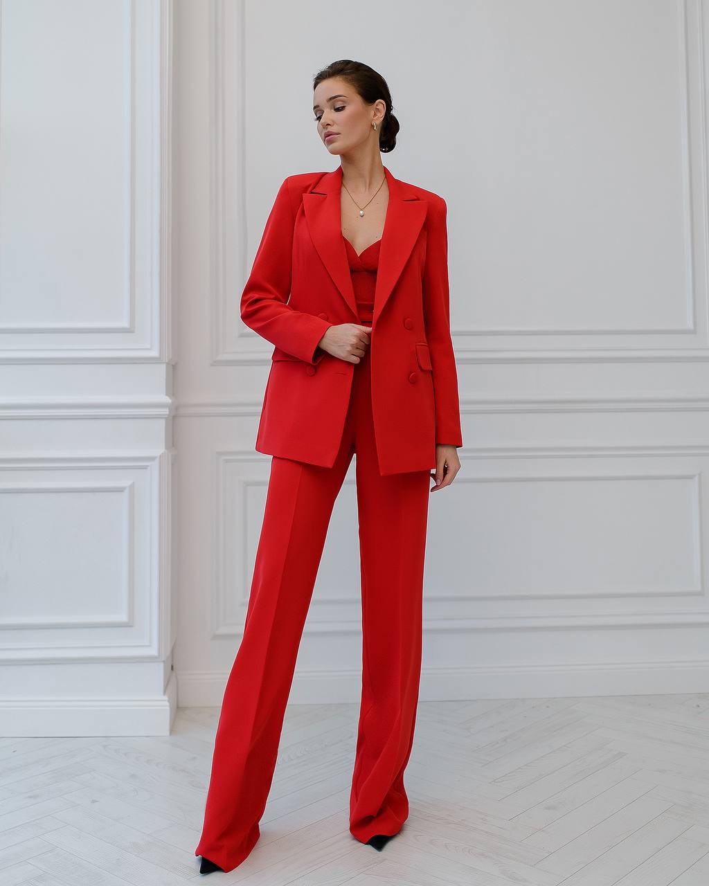 Woman wearing a red suit standing against a white paneled wall.