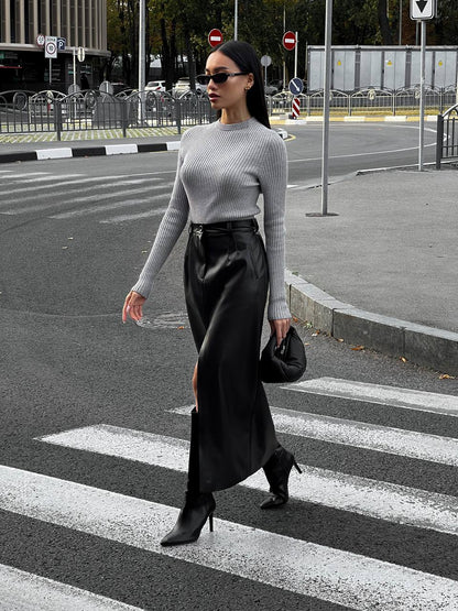 Woman crossing a street wearing a gray sweater and black skirt.